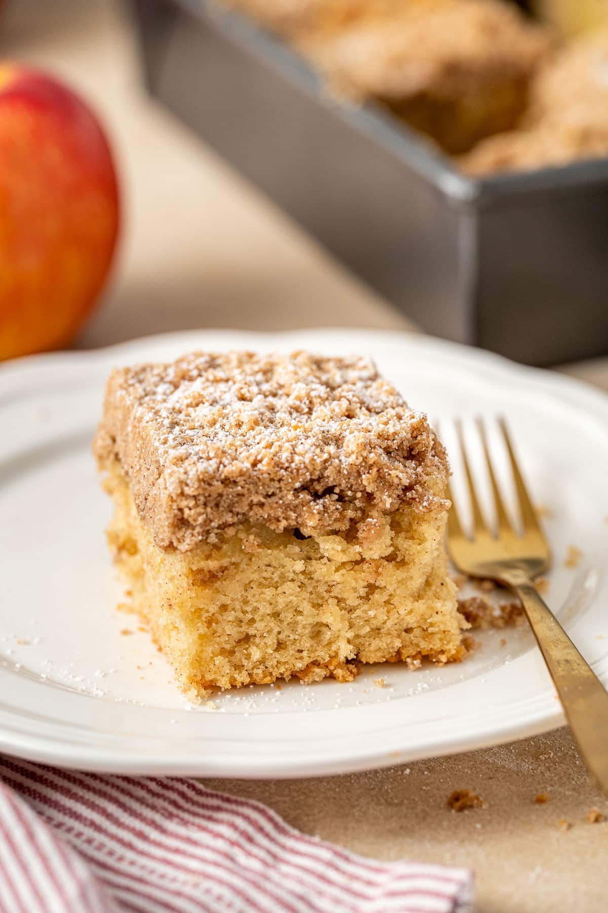 Close-up view of a slice of Cinnamon Apple Coffee Cake dusted with powdered sugar and a golden fork beside it.